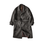 A Men's Woolen Balmacaan Coat in a charcoal gray color with a single chest pocket, waist pockets, and a button closure. It features a windproof tap at the neck and horn buttons.