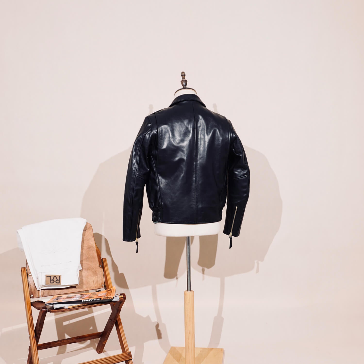 Black leather jacket on a mannequin with a wooden chair and white towel in the background