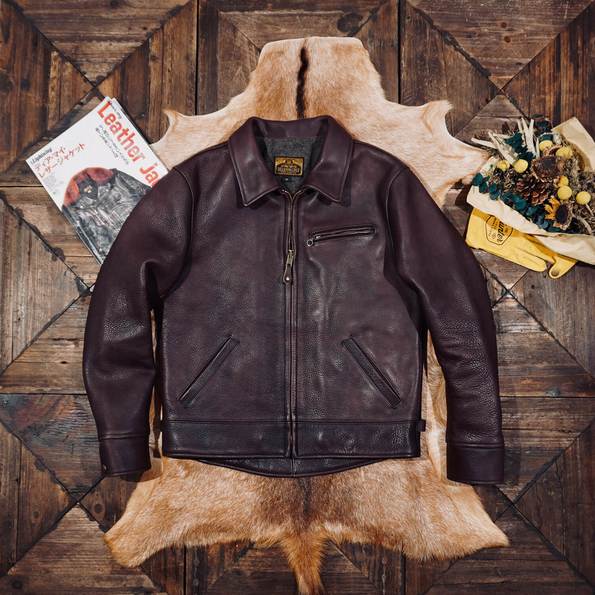 Brown leather jacket on a wooden surface with a magazine and decorative items.