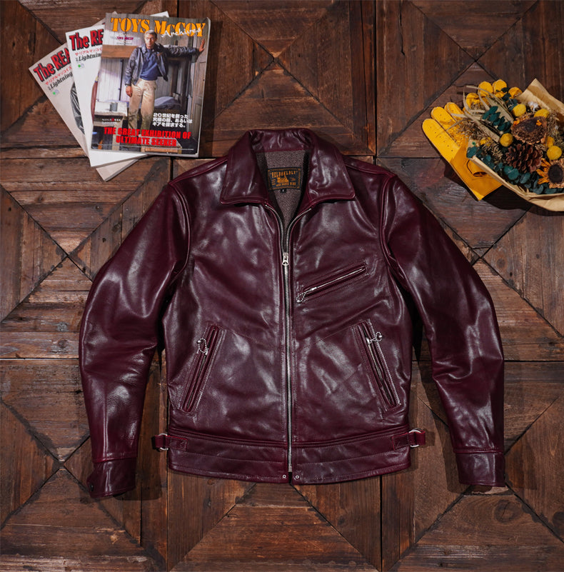 A black leather jacket with a slim vintage fit, open collar, zip front closure, three zippered pockets, and adjustable brass buckles at the back.