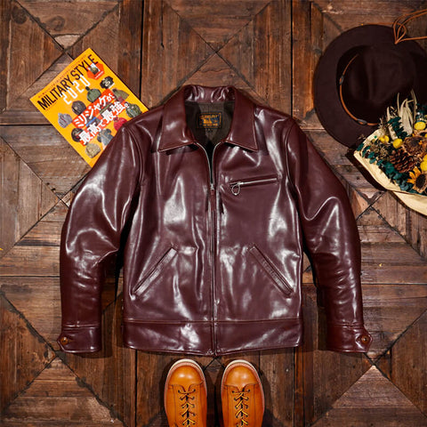 Brown leather jacket on a wooden surface with a hat and magazine in the background