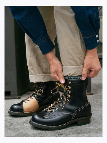 Person wearing black leather boots with a unique design, standing on a concrete surface.