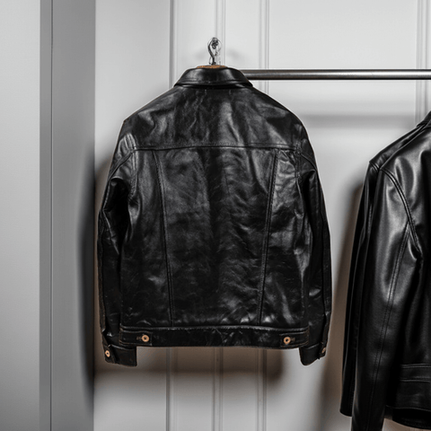 Black leather jacket hanging on a rack against a white paneled wall.